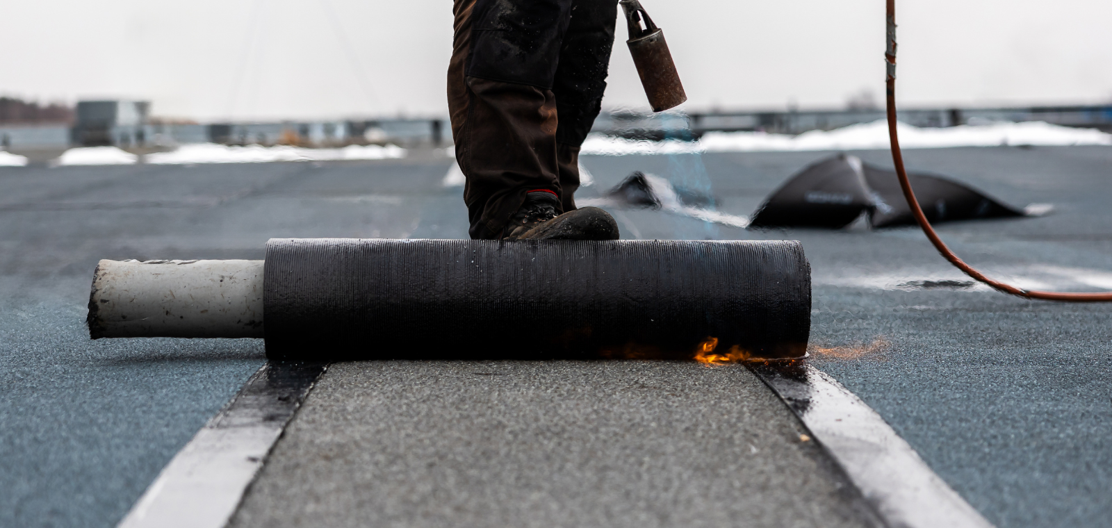 Roofer installing EPDM rubber membrane on a flat roof in Massachusetts